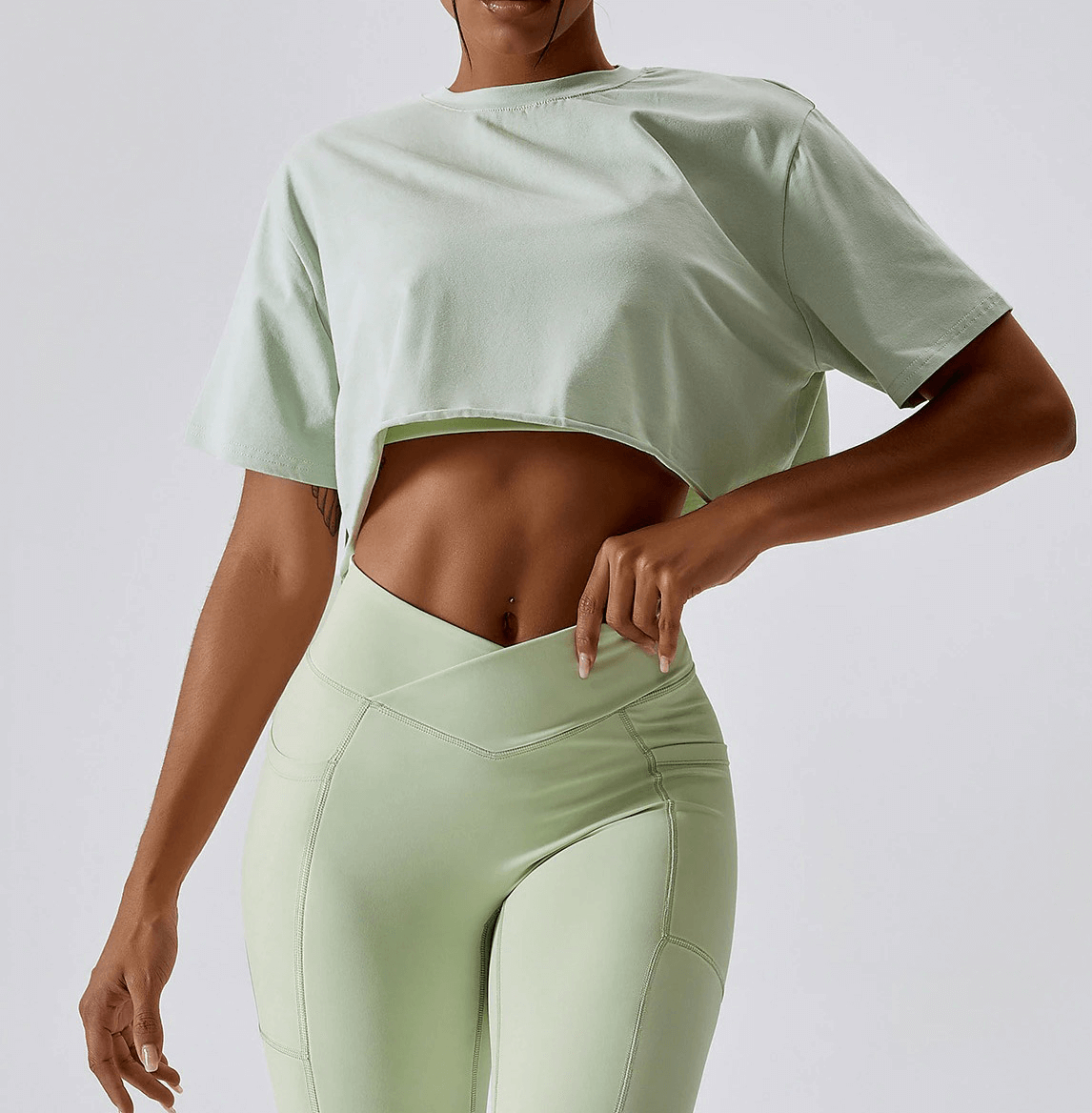 Woman in mint green sports loose crop top and leggings, ideal for yoga and running. O-neck, breathable polyester-spandex.